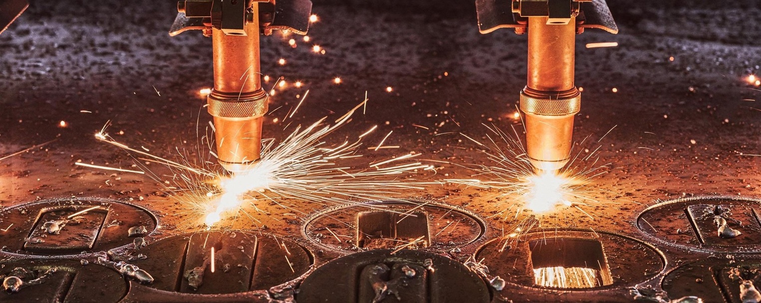 Zwei industrielle Plasmaschneidbrenner sprühen helle Funken, während sie in einer Fabrikhalle Metallbleche durchschneiden.