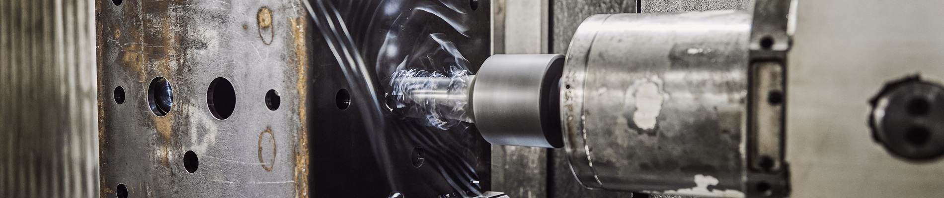 Nahaufnahme einer CNC-Maschine, die in einen Metallblock bohrt, mit sichtbaren Löchern und Metallspänen, in einer industriellen Umgebung.