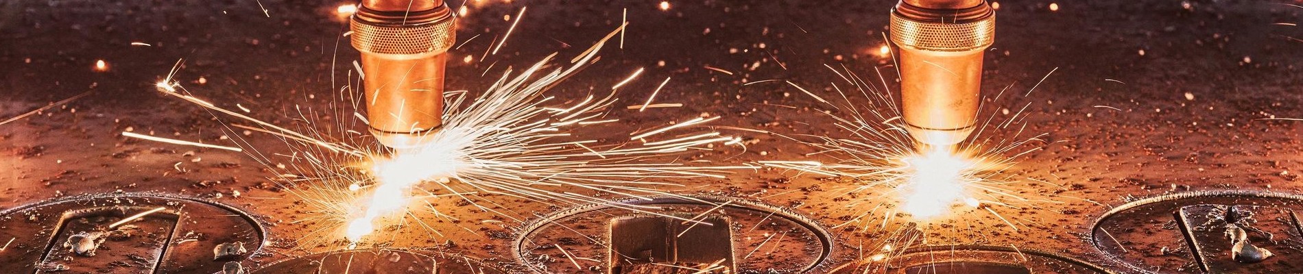 Two industrial plasma cutters emitting bright sparks, cutting through metal sheets, surrounded by scattered metal debris.