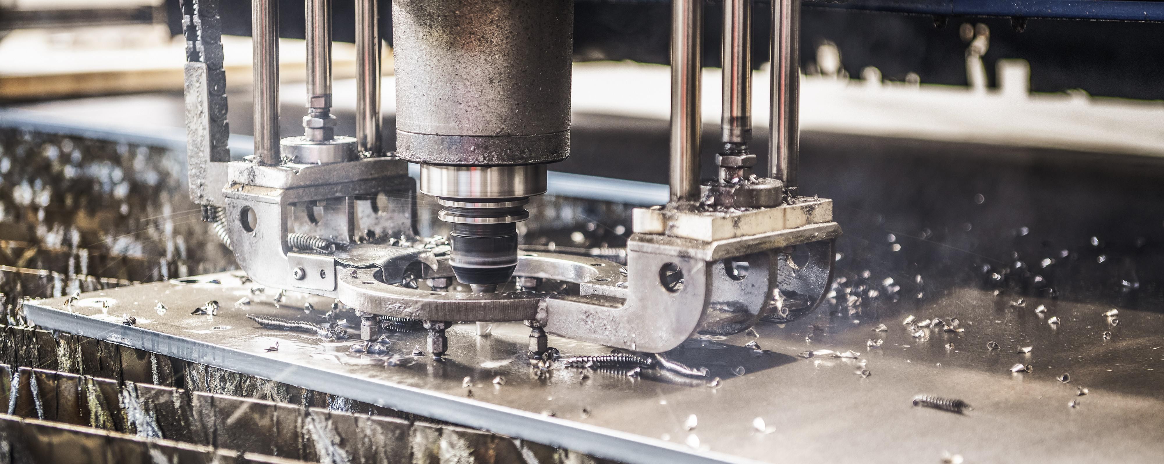 CNC-Frässpindel beim Schneiden einer Metallplatte, die in Vorrichtungen mit verstreuten Metallspänen und Kühlmittel eingespannt ist.