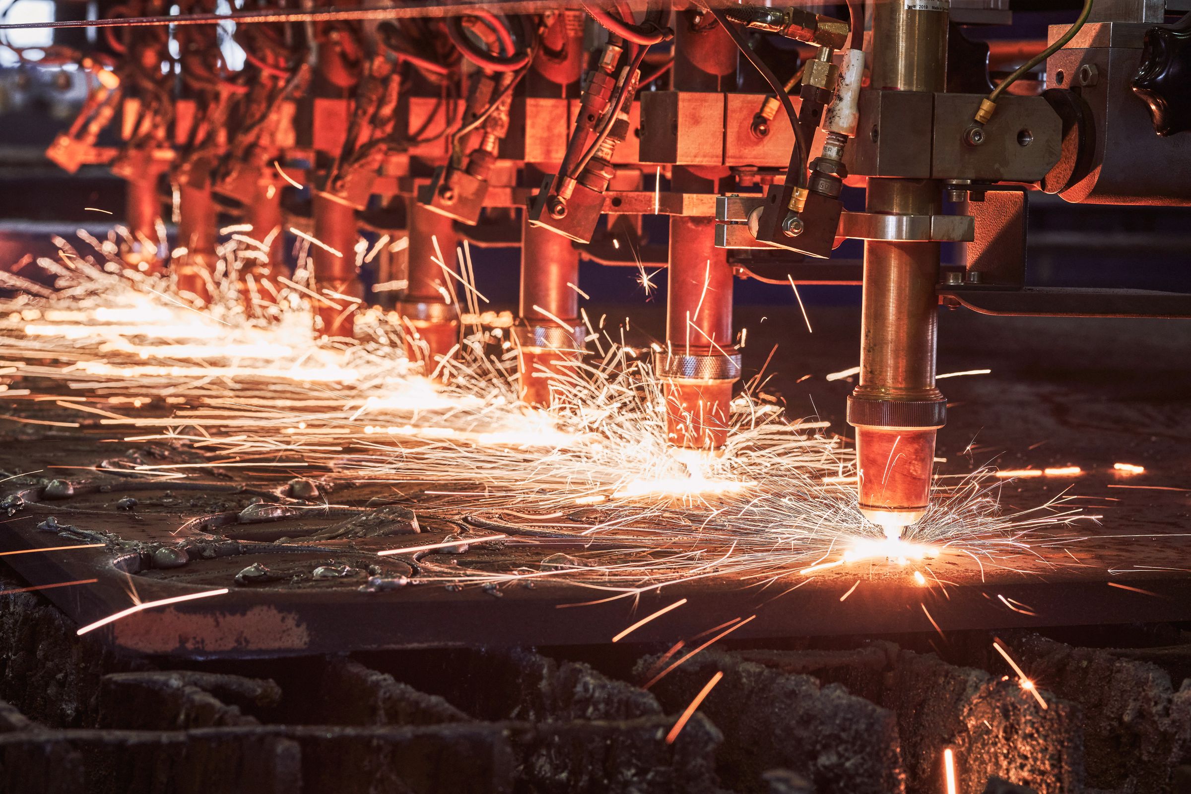 Industrielle Metallbearbeitung, bei der Funken aus mehreren CNC-Plasmabrennern sprühen.