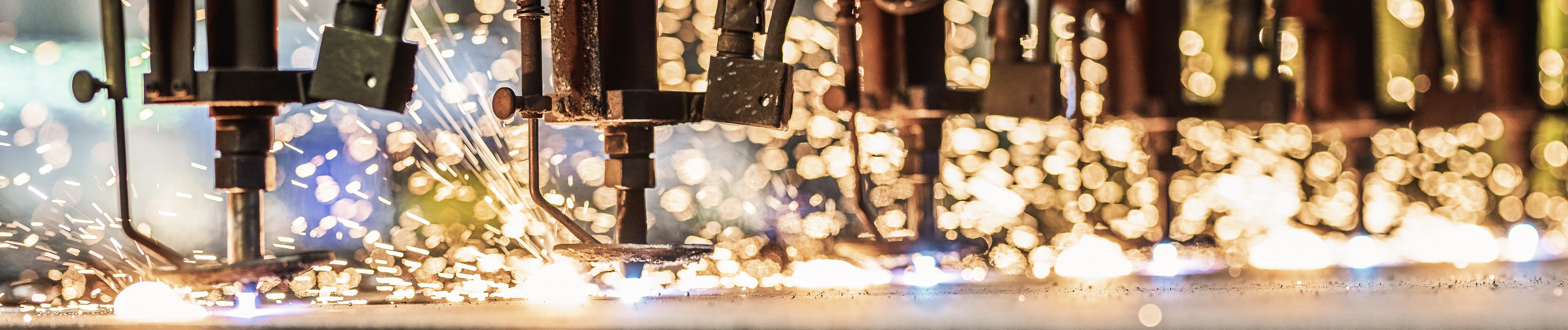 Nahaufnahme von industriellen Maschinen, Funkenregen und hellen Bokeh-Lichtern.