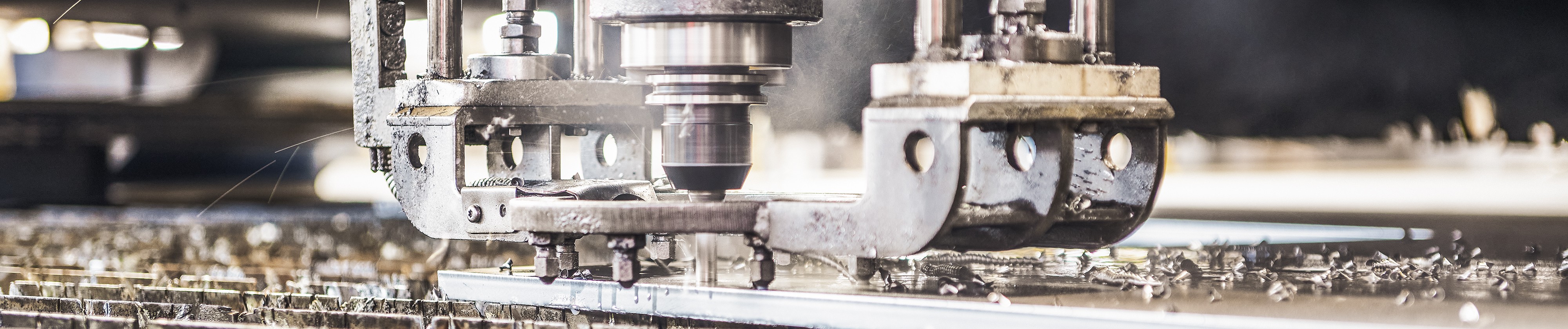 Nahaufnahme einer Maschine, die ein Blech schneidet, wobei Metallspäne umherfliegen.