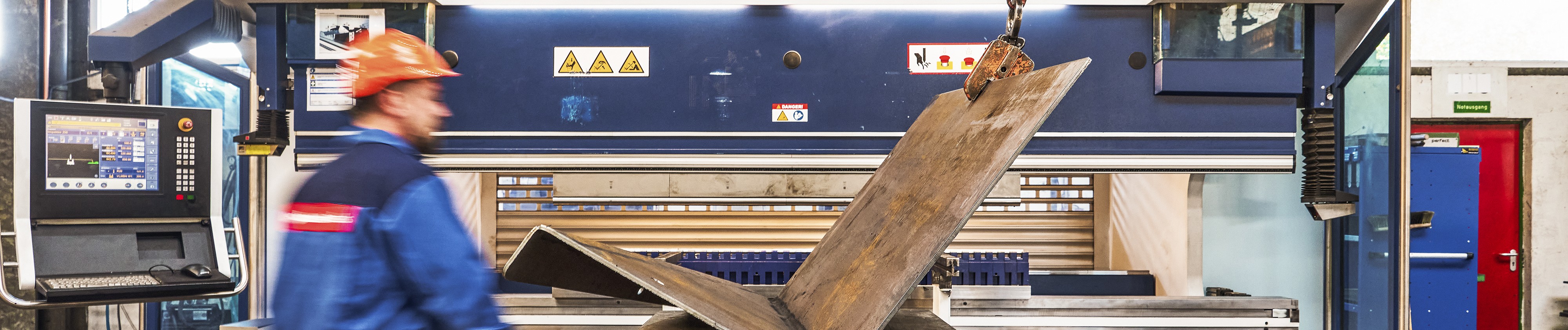 Arbeiter in einem Servicecenter, der eine große Maschine bedient, mit einem Computer-Bedienfeld in der Nähe.