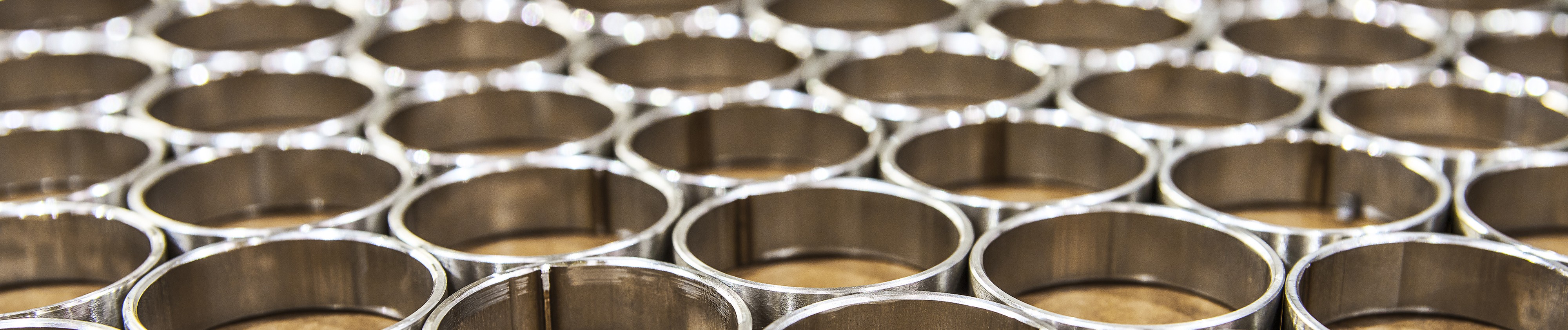 Nahaufnahme von polierten zylindrischen Metallringen (Hohlrohren), die in einem sich wiederholenden Gittermuster angeordnet sind.
