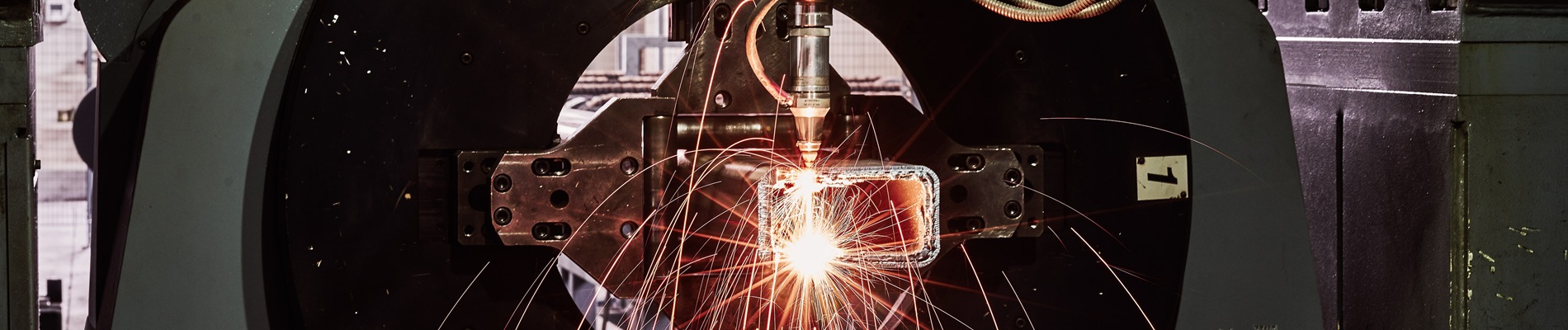 A machine performing laser cutting on a metal object, with bright sparks flying around in an industrial setting.