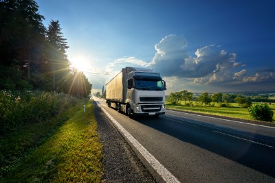 White truck arriving on the asphalt road in rural landscape in the rays of the sunset